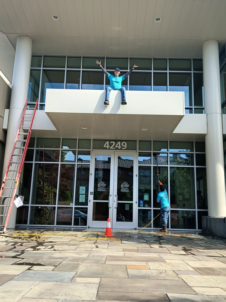 Window cleaning technician with a water-fed pole and ladder cleaning windows at Elks Lodge Palo Alto