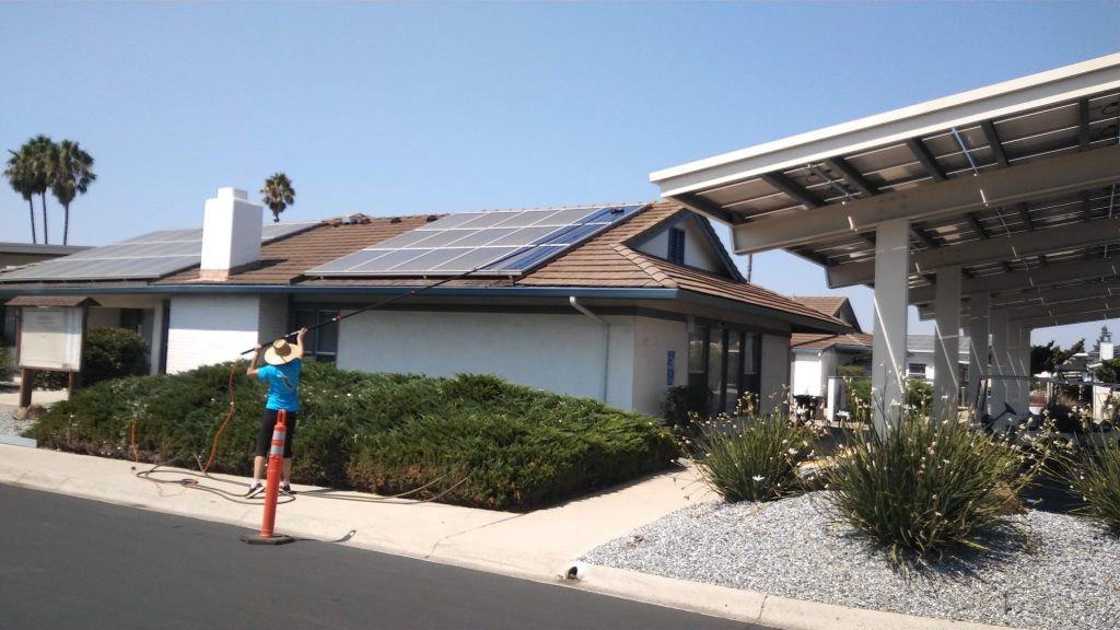 Technician cleaning rooftop solar panels with water-fed pole